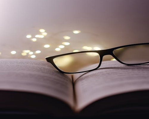 Warm indoor lighting illuminating an open book and reading glasses