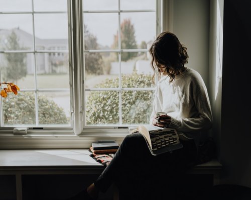 Person reading a book next to a window with soft natural light